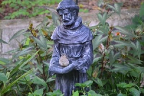 bluebird fledgling sitting on statue of a saint in a garden